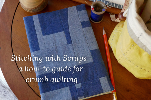 A Making eBook journal cover is on a journal laying on a wooden table, pieced from a variety of blue scraps. The title "Stitching With Scraps - a how-to guide for crumb quilting" is layered on top.